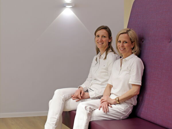 Dr. Kühn und Dr. Böttcher sitzen nebeneinander und blicken freundlich in die Kamera.